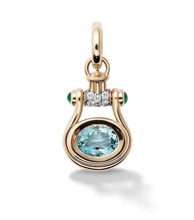 A gold pendant charm featuring a large oval light blue gemstone, accented by a curved top loop, a row of small clear stones, and two tiny green gemstones on either side, shown on a white background.