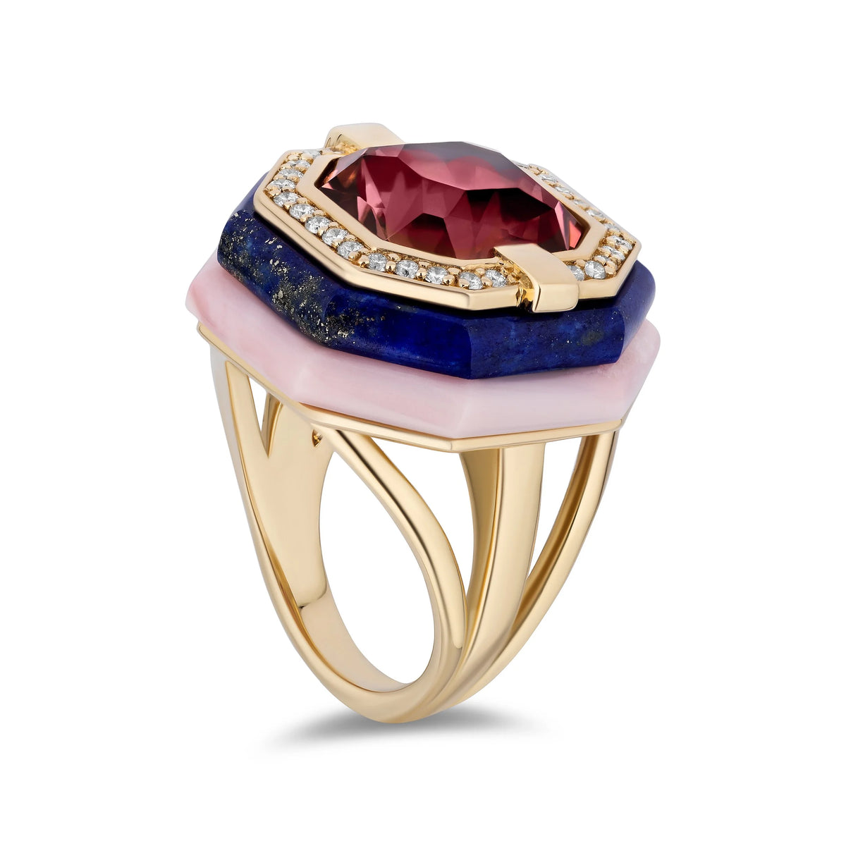 A gold ring featuring a large faceted pink gemstone, a dark blue lapis lazuli stone, and a light pink stone, accented with small clear crystals in a gold bezel setting.