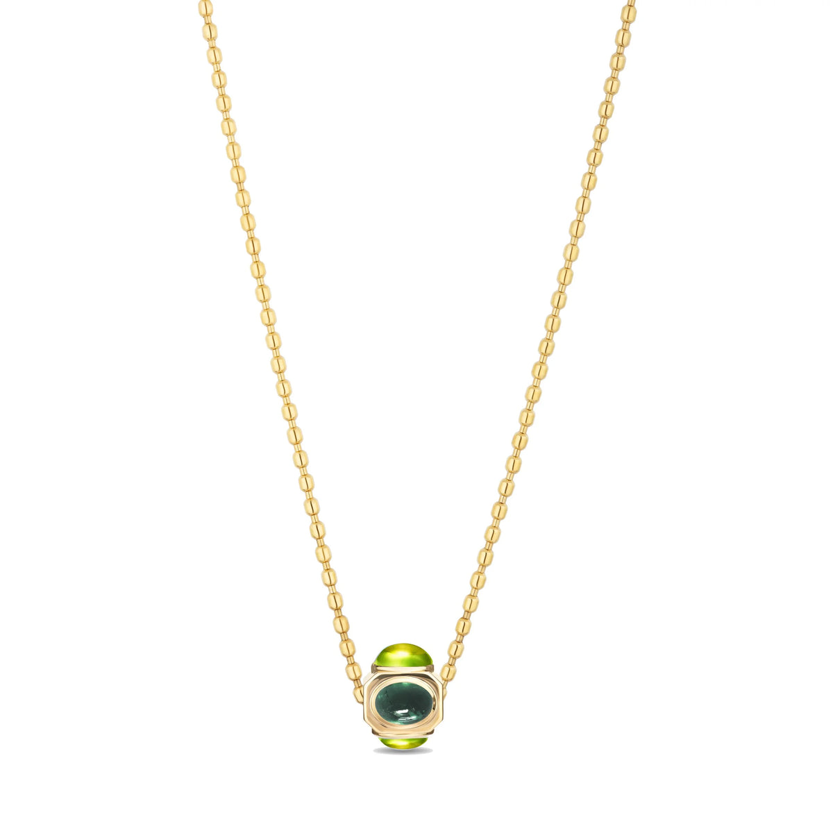 A delicate gold chain necklace featuring a bead with a bright green stones and a dark green window, set against a plain white background.