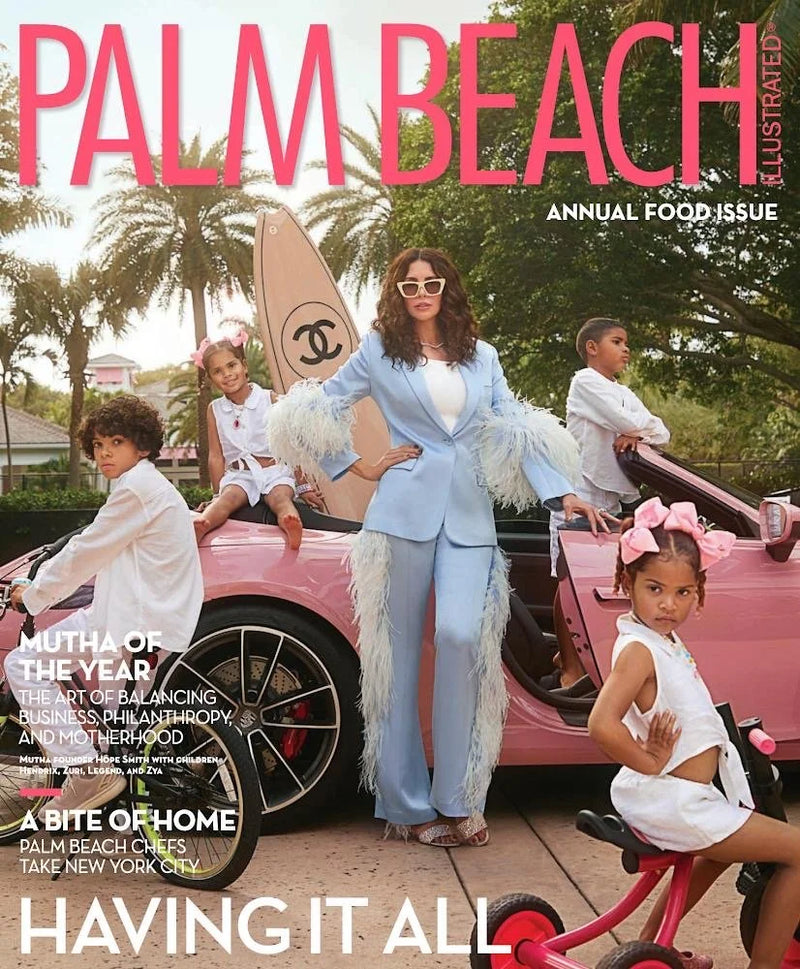 A woman in a light blue suit with feathered details standing in front of a pink sports car with four children sitting or standing around her, outdoors with palm trees and greenery in the background, on the cover of Palm Beach magazine.