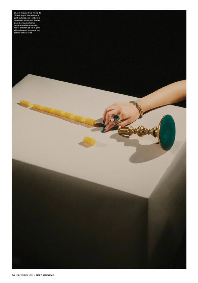 A display of jewelry and objects on a table, including a hand with turquoise and gold jewelry, yellow puzzle pieces, and a brass candlestick.