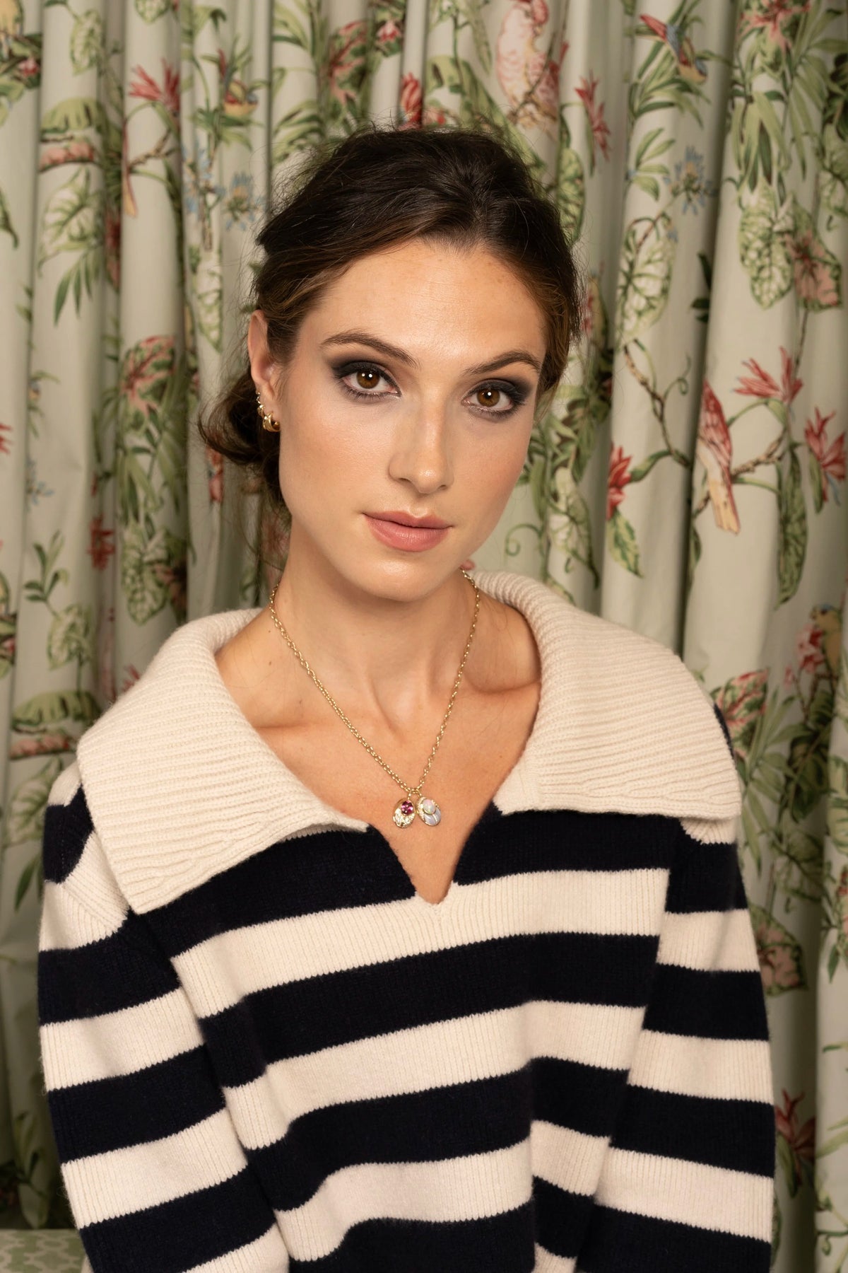 A woman wearing a cream and navy horizontally striped knit sweater with a wide ribbed collar, posed in front of a floral curtain.
