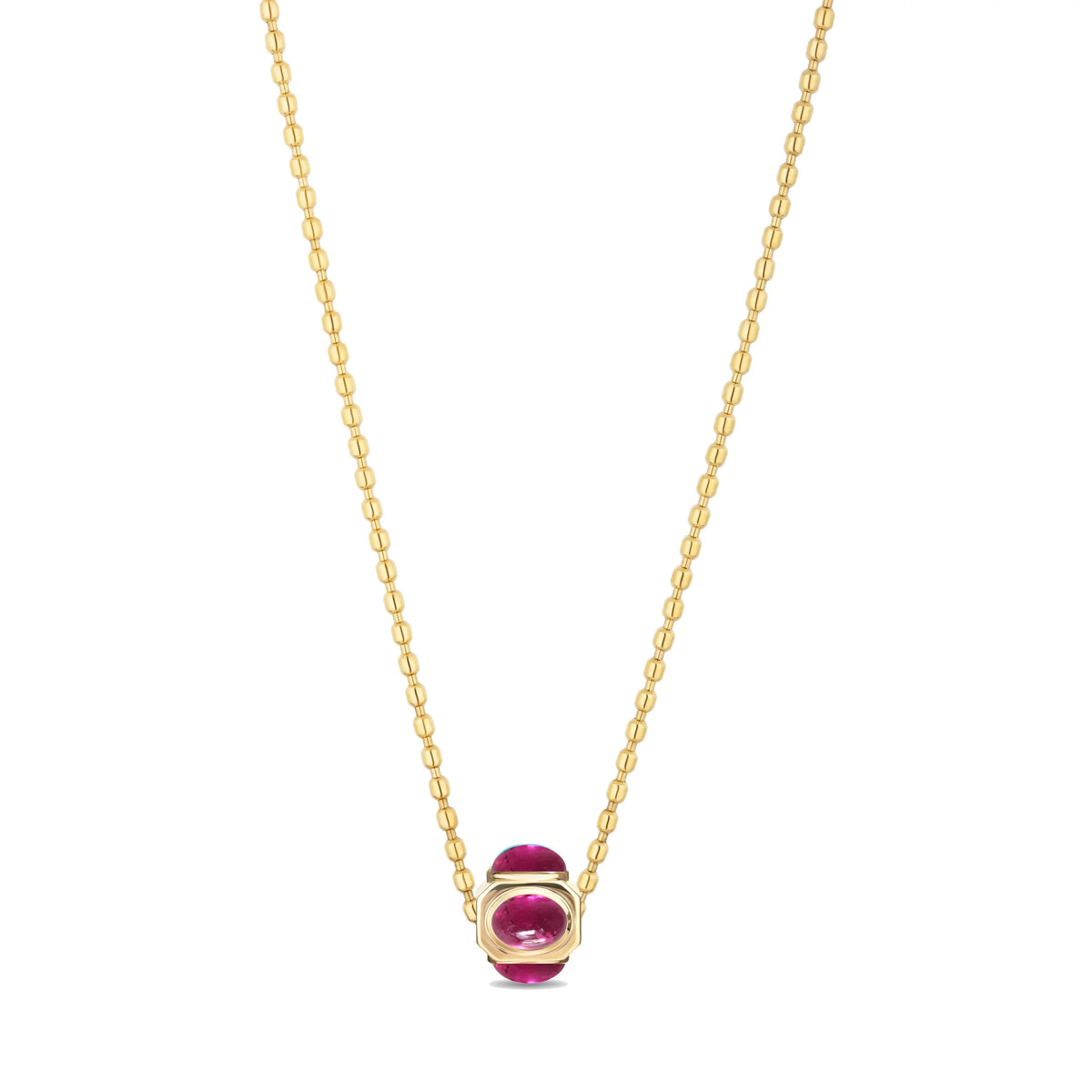 A delicate gold chain necklace featuring a small oval-cut pink gemstone in a gold bezel setting, displayed against a solid white background.