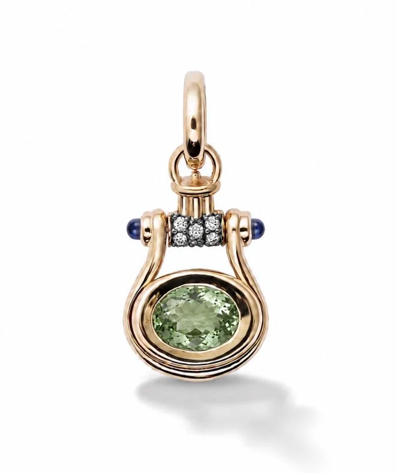 A gold pendant featuring a large oval-cut light green gemstone, accented by a row of small clear stones and two dark blue round gemstones on either side, set against a plain white background.