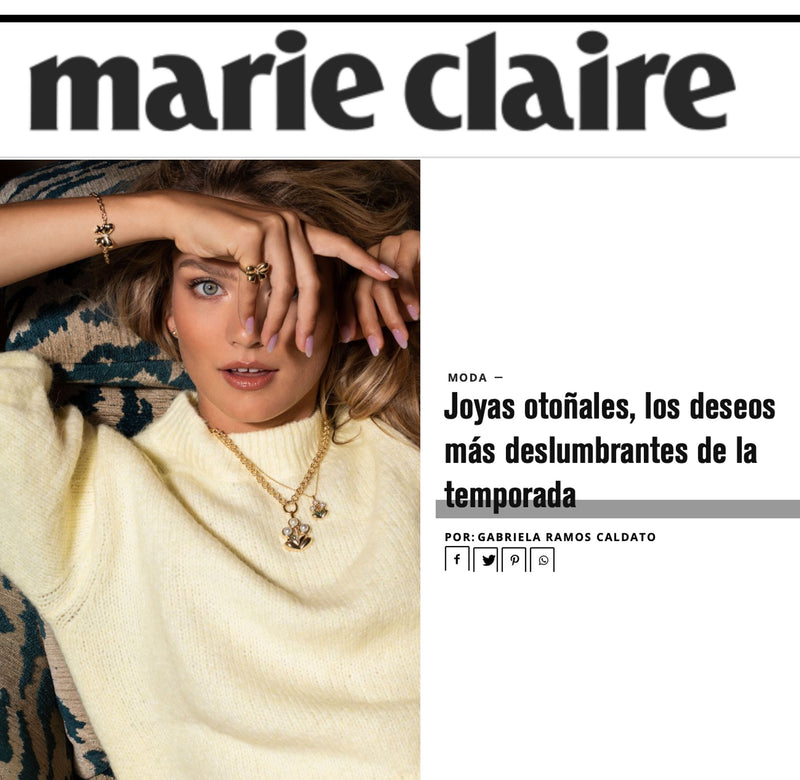 A woman with light skin and blue eyes lying down, covering one eye with her hand, wearing a cream-colored sweater and gold jewelry.