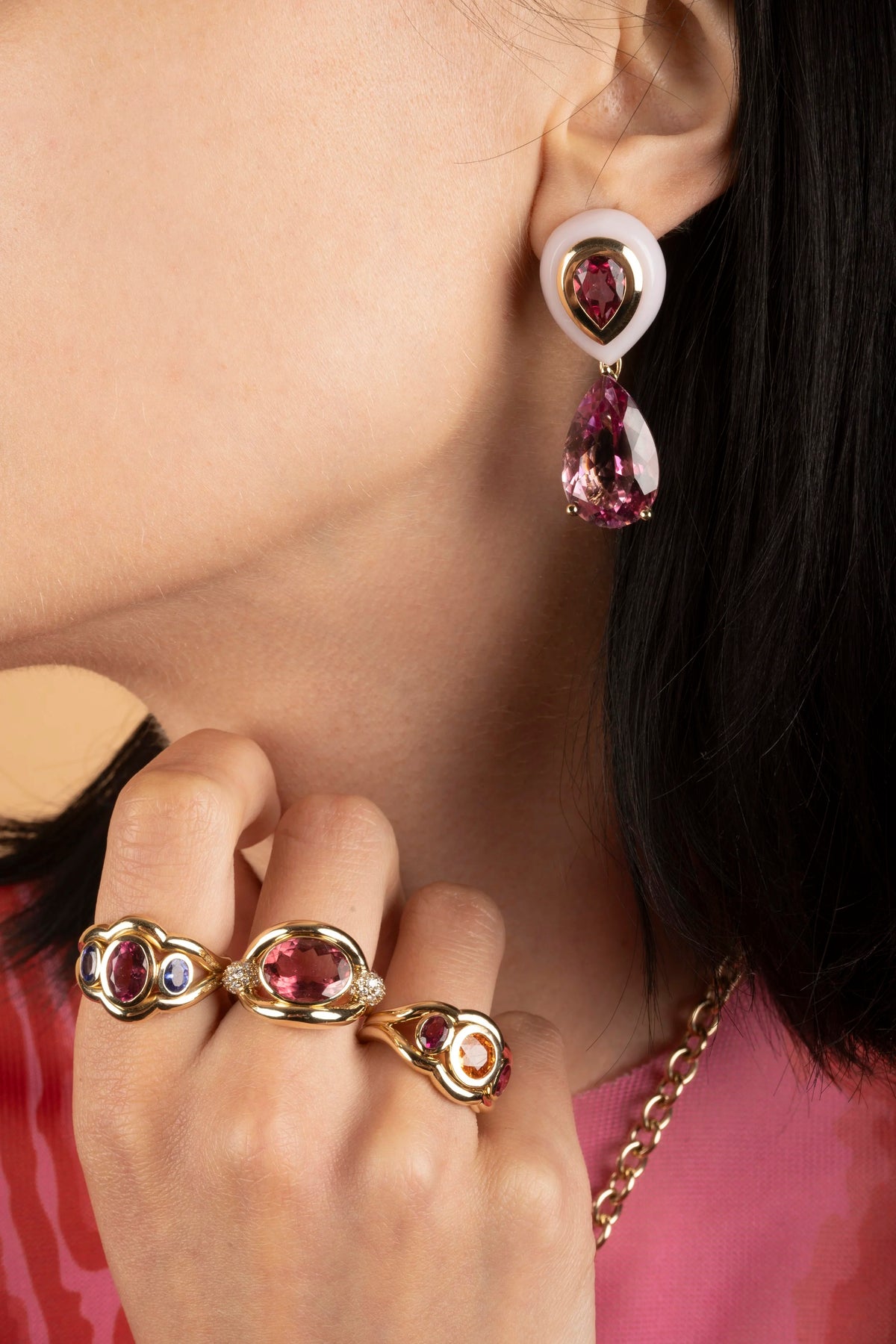 A close-up lifestyle shot of a model wearing a matching jewelry set featuring gold rings and an earring with teardrop-shaped pink gemstones.