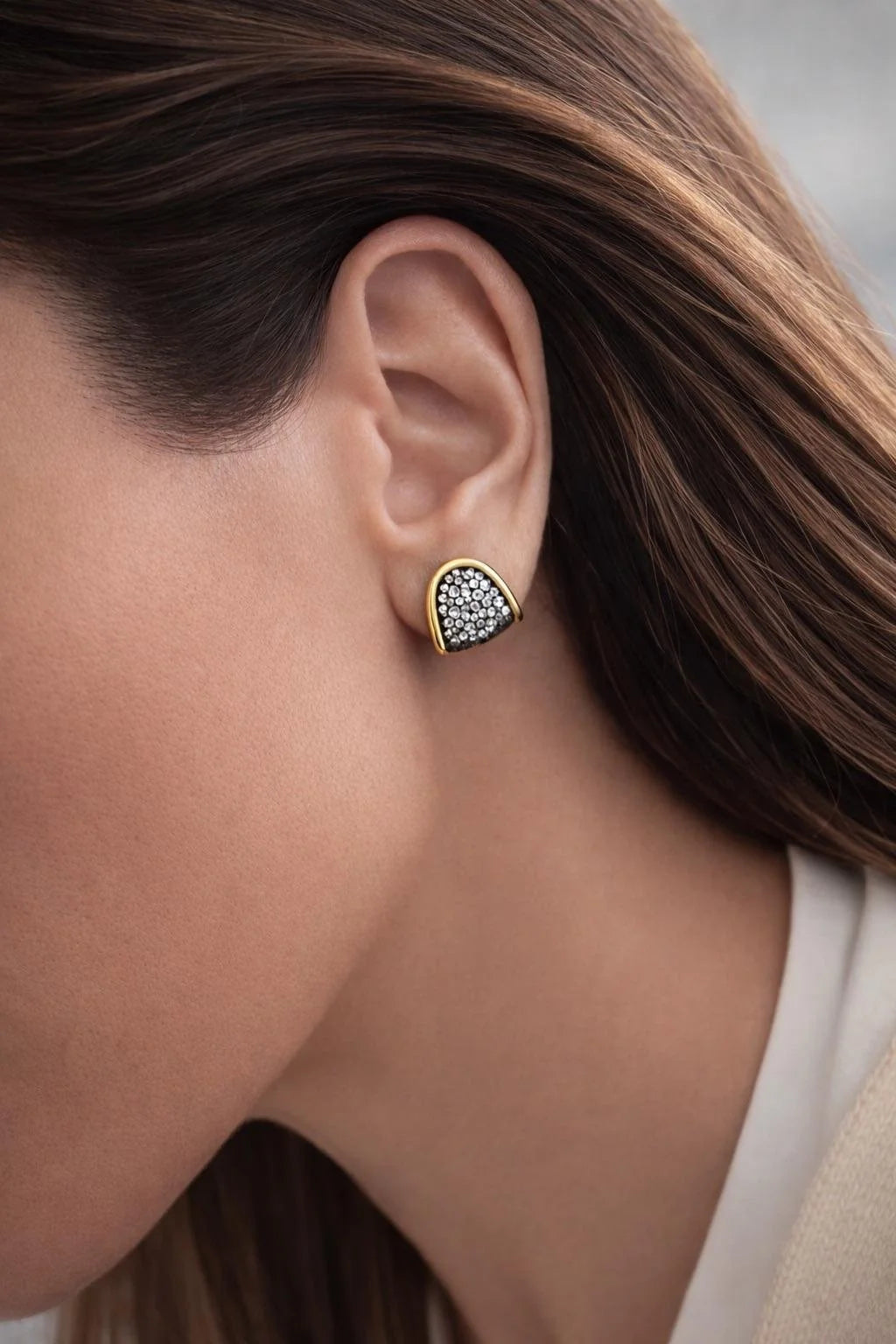 A close-up of a woman's ear wearing a teardrop-shaped stud earring with a gold border and a pavé-set black and white stone center.