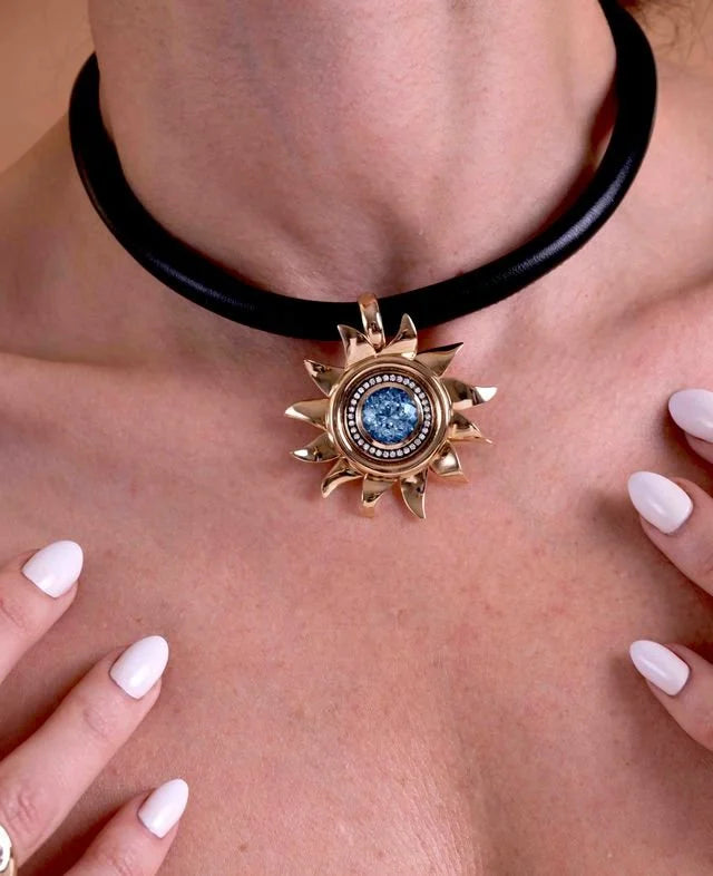A close-up of a person wearing a black choker necklace with a gold sunburst pendant featuring a central blue gemstone.